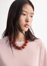 Collar corto de cuentas esféricas grandes en tonos rojizos marmoleados, con cierre de cadena metálica y mosquetón.