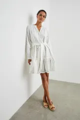 Vestido corto blanco de algodón con bordados calados, cuello en V, mangas largas con puños elásticos y cinturón de lazo.