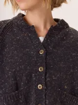 Saco de lana color marrón, de tejido grueso, con cuello redondo y botones frontales. Presenta mangas raglán con detalle de punto acanalado y bolsillos delanteros tipo parche.