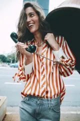 Camisa de manga larga con estampado de rayas verticales en color naranja y crema. Presenta cuello solapa, cierre frontal con botones dorados y puños anchos en color crema con detalle de lazos ajustables.