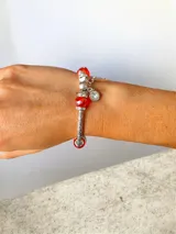 Pulsera elástica de estructura plateada con cuentas de cristal en color rojo y dijes colgantes, incluyendo un dije de mariposa y un dije de cristal tipo punto de luz.