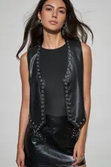 Chaleco negro de cuero sintético con escote en V y ojales metálicos decorativos a lo largo de los bordes delanteros y el dobladillo.
