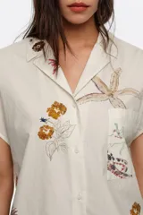 Camisa de manga corta color blanco con cuello solapa y estampado de temática marina con peces y estrellas de mar, con cierre frontal de botones y un bolsillo en el pecho.