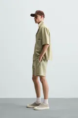 Bermuda de algodón color blanco, de corte relajado (relaxed fit), con cintura elástica ajustable mediante cordón. Posee bolsillos laterales y un bolsillo trasero de plastrón. Presenta un bordado en contraste en la pernera.