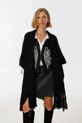Ruana negra de tejido de punto con flecos y aplique de cuero vacuno con manchas blancas.
