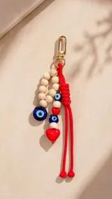 Cartera tipo hobo de cuero sintético color suela, con interior espacioso y costuras decorativas frontales. Incluye asa de hombro fija, monedero rectangular colgante a juego y un llavero amuleto con cuentas de madera, ojos turcos y detalles en rojo.