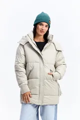 Campera puffer larga con capucha, color beige, de ajuste relajado. Presenta cierre frontal con botones a presión, bolsillos laterales con cierre y puños tejidos acanalados.