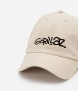 Gorra de béisbol color beige con bordado del logo de la banda Gorillaz en negro.