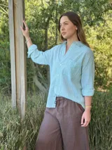 Camisa celeste a rayas verticales blancas, de corte holgado, manga larga con puños abotonados, cuello camisero y bolsillo en el pecho.