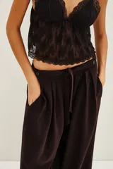 Pantalón de corte sastrero y pierna ancha, color marrón oscuro, con pinzas en la cintura y cierre frontal con lazo ajustable.