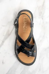 Sandalia de cuero color negro charol, con tiras cruzadas y hebilla ajustable al tobillo. Plataforma con suela track.