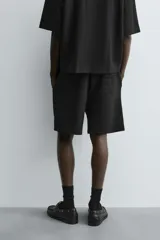 Bermuda de corte relajado color marrón con finas rayas verticales negras. Presenta cintura elástica ajustable con cordón y bolsillos laterales y trasero.