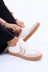 Championes casuales de color blanco con detalles en beige y suela de goma marrón. Presentan diseño clásico con cordones y apliques laterales en zig-zag.