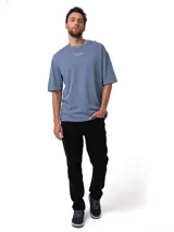 Remera de algodón con textura slub, color azul grisáceo, de corte relajado y cuello redondo. Presenta un gráfico bordado pequeño en el centro del pecho y parche con logo en la manga.