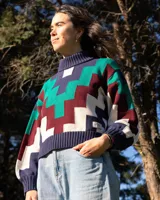 Sweater de cuello alto tejido con diseño geométrico en zigzag multicolor, incluyendo tonos azul marino, verde, bordó y crema. Presenta puños y ruedo acanalados.