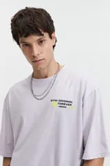 Remera oversize color marrón claro con estampado gráfico en la espalda que incluye frases como "Stay Original Forever", "All About Having Fun" y el logo de Mistral, junto con otros garabatos y stickers.