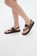 Sandalias de cuero sintético color marrón, con diseño de tiras cruzadas estilo ojota, capellada con hebilla metálica dorada decorativa y tira trasera ajustable con hebilla.