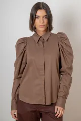 Camisa de algodón color marrón con mangas largas abullonadas, cuello clásico y cierre frontal oculto. Presenta botones decorativos con strass en los puños y en el cuello.