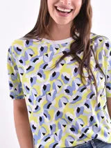 Remera de manga corta color beige con estampado de bananas en tonos amarillo, naranja y rosado.