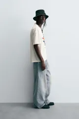 Camiseta de manga corta y cuello redondo, color blanco hueso, con un estampado abstracto multicolor en el pecho que incluye texto en la parte inferior.