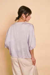 Blusa de satén color lila con escote en V y cierre frontal con botones.