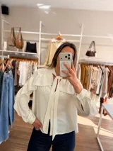Camisa de color rojo intenso con volados en los hombros y lazo ajustable en el cuello. Presenta un cierre frontal con botones y un diseño de calce amplio.