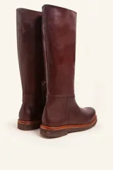 Bota de caña alta confeccionada en cuero vacuno suave, con diseño minimalista y suela de goma robusta. Presenta costuras visibles en la zona del empeine y un taco bajo cuadrado.