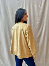 Chaqueta color beige con cuello redondo, cierre frontal con botones a presión, bolsillos de parche y mangas largas.