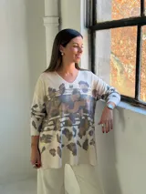 Sweater de punto con escote en V y mangas largas, de diseño holgado. Presenta un estampado animal print abstracto en tonos chocolate y detalles metalizados en color dorado sobre una base color crema.