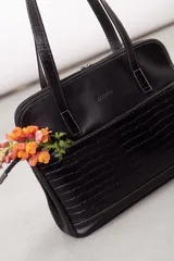 Cartera de hombro tipo portafolio confeccionada en cuero vacuno, con diseño estructurado que combina marrón liso y un panel frontal en cuero texturizado color mostaza. Posee doble asa larga y cierre superior.