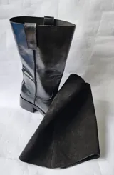 Bota de cuero negro con diseño 2 en 1, que incluye una polaina de gamuza desmontable. Presenta una base de bota de cuero liso y una caña alta de gamuza, ofreciendo versatilidad para diferentes estilos.