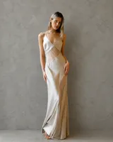 Vestido largo de satén color champagne, con escote en V profundo, tirantes finos y recortes geométricos laterales que estilizan la silueta.