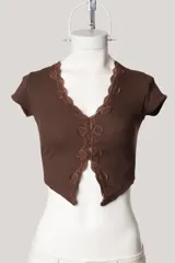 Remera de tejido acanalado color beige, con escote en V profundo decorado con puntilla de encaje en los bordes, mangas cortas y diseño abierto en el frente.