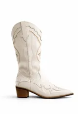 Bota estilo texana de caña alta, color blanco, con bordados decorativos en el cuerpo y en la puntera. Presenta un taco cuadrado de madera y punta fina.