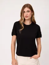 Remera negra de manga corta con vuelta en los puños y detalle de botones dorados. Cuello redondo.