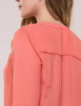 Blusa de calce relajado color salmón, confeccionada en tela liviana con textura sutil. Presenta escote en V con abotonadura frontal, bolsillo parche en el pecho, mangas largas regulables con presilla y ruedo con opción de anudar en el frente.
