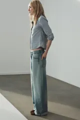 Jeans de tiro medio con cinco bolsillos, trabillas y cierre frontal con cremallera y botón metálico. Presenta un diseño baggy con piernas anchas, roturas decorativas y dobladillo vuelto en los bajos.