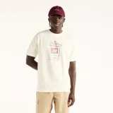 Remera New Balance de hombre, color blanco off-white, con corte amplio y estampa frontal de estilo pixelado en tono bordó con la silueta de un champión sobre una pantalla.
