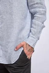 Camisa de manga larga para hombre, con cuello clásico y botones frontales. Presenta un estampado de rayas verticales finas en tonos azul claro y blanco.