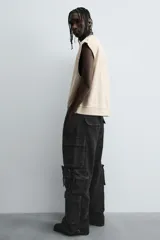 Pantalón cargo de denim lavado negro, corte relajado y tiro medio. Presenta múltiples bolsillos cargo con solapa y detalle de cierre en las perneras, además de bolsillos de vivo traseros. El bajo es ajustable con trabilla.