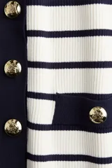 Cárdigan corto de punto acanalado en mezcla de viscosa, con rayas horizontales blancas y azul marino. Presenta cuello redondo ribeteado en azul marino, cierre frontal con botones dorados y bolsillos insertados decorativos con botón dorado. Tiene mangas cortas.