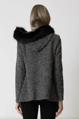 Abrigo de lana bouclé en blanco y negro, con corte recto, bolsillos amplios y cierre metálico frontal. Detalle de piel sintética negra en los hombros.