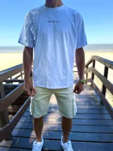 Remera oversize de color beige con estampa en la espalda de una palmera y una tabla de surf, acompañada de la inscripción "Surfer's Paradise Laguna Beach".
