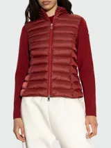Cardigan híbrido de Moncler con frente acolchado tipo puffer en color bordó y mangas de punto de lana virgen al tono. Presenta cierre frontal completo y cuello alto.
