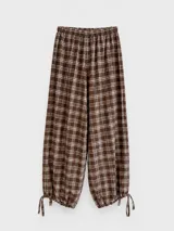 Pantalón de corte balloon con estampado cuadrillé en tonos marrones. Presenta cintura elastizada y terminaciones en los tobillos con tiras ajustables para anudar, creando un efecto bombé.