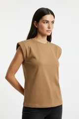 Remera de algodón color tostado, con cuello redondo a la base y hombreras marcadas que le otorgan una estructura definida.