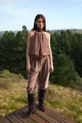 Blusa sin mangas de corte holgado con cuello alto tipo halter y pliegues frontales. Confeccionada en tela con textura sutil.