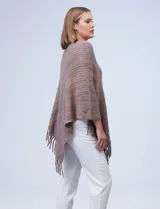 Poncho tejido en hilo soft, con efecto jaspeado multicolor (predominantemente tonos oscuros como azul marino, negro, y toques de violeta y dorado/lurex). Presenta un diseño asimétrico y flecos largos en los bordes.