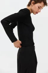 Saco de punto acanalado negro de manga larga, con cuello redondo y cierre frontal de múltiples botones.
