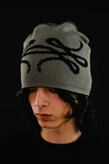 Beanie reversible tejido en algodón, con diseño gráfico abstracto. Presenta un lado en color negro con estampa gris y el otro lado en color gris con estampa negra. Incluye etiqueta de marca en el borde inferior.